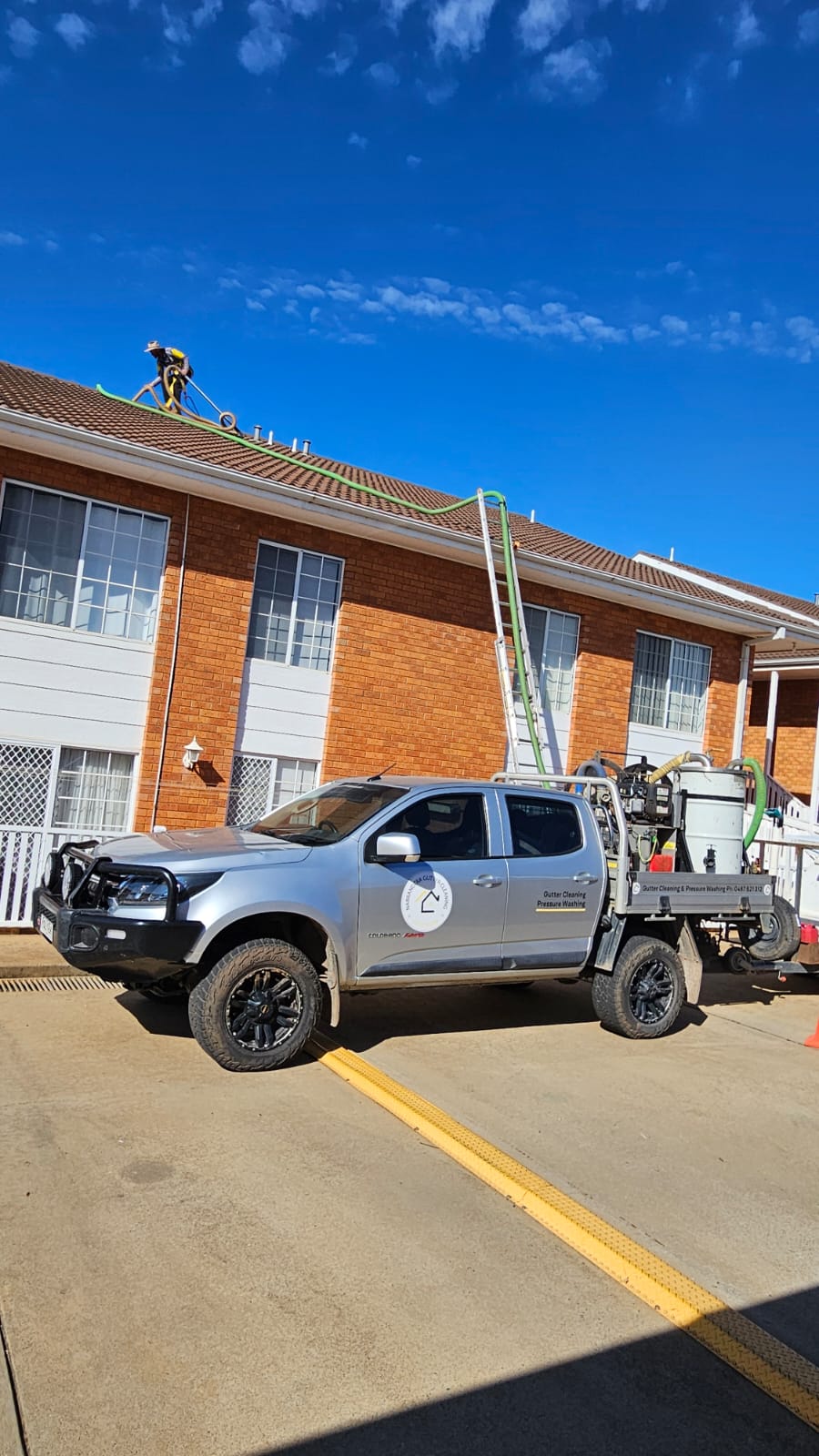 Industrial gutter vacuum system hose reaching high-pitch roof track