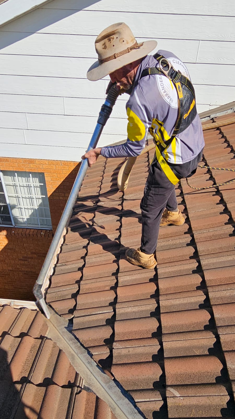 Expert gutter cleaner vacuuming dry leaves and twigs from brick roof valleys