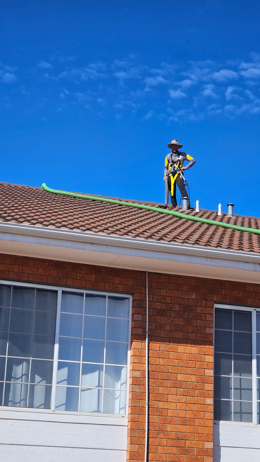 Licensed professional gutter cleaner wearing safety harness compliant gear